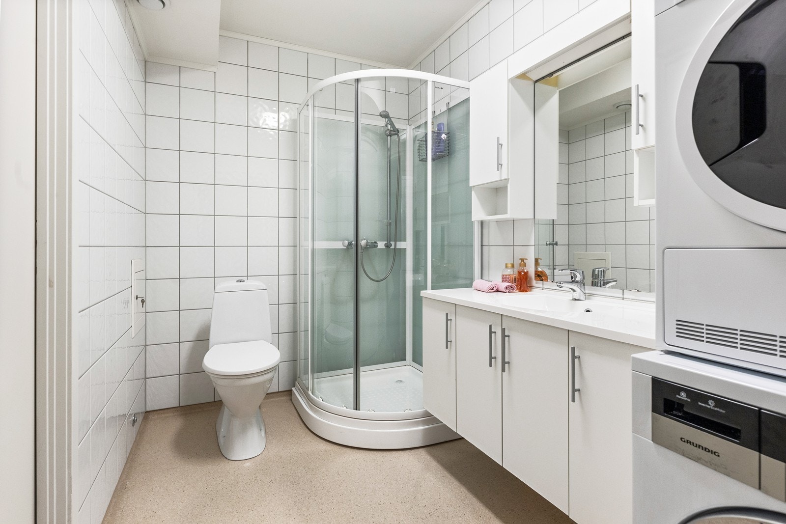 Badet/vaskerommet fra byggeåret kombinerer funksjonalitet med stil, utstyrt med nedfelt servant, gulvfestet toalett, dusjkabinett, og opplegg for vaskemaskin, for en praktisk og effektiv hverdag. Galleribilde