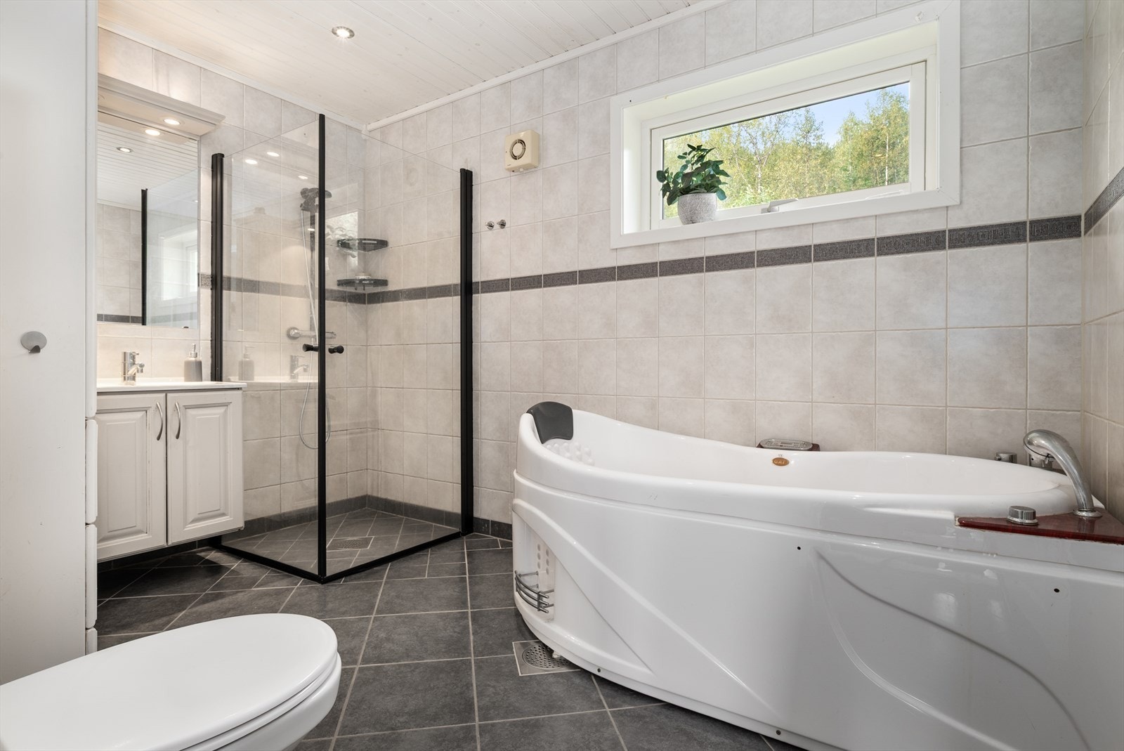 Flislagt bad med behagelig varme i gulvet. Innredning med 2 servanter og heldekkende vask/benkeplate, innsvingbare dusjdører, vegghengt toalett og boblebadekar. Galleribilde