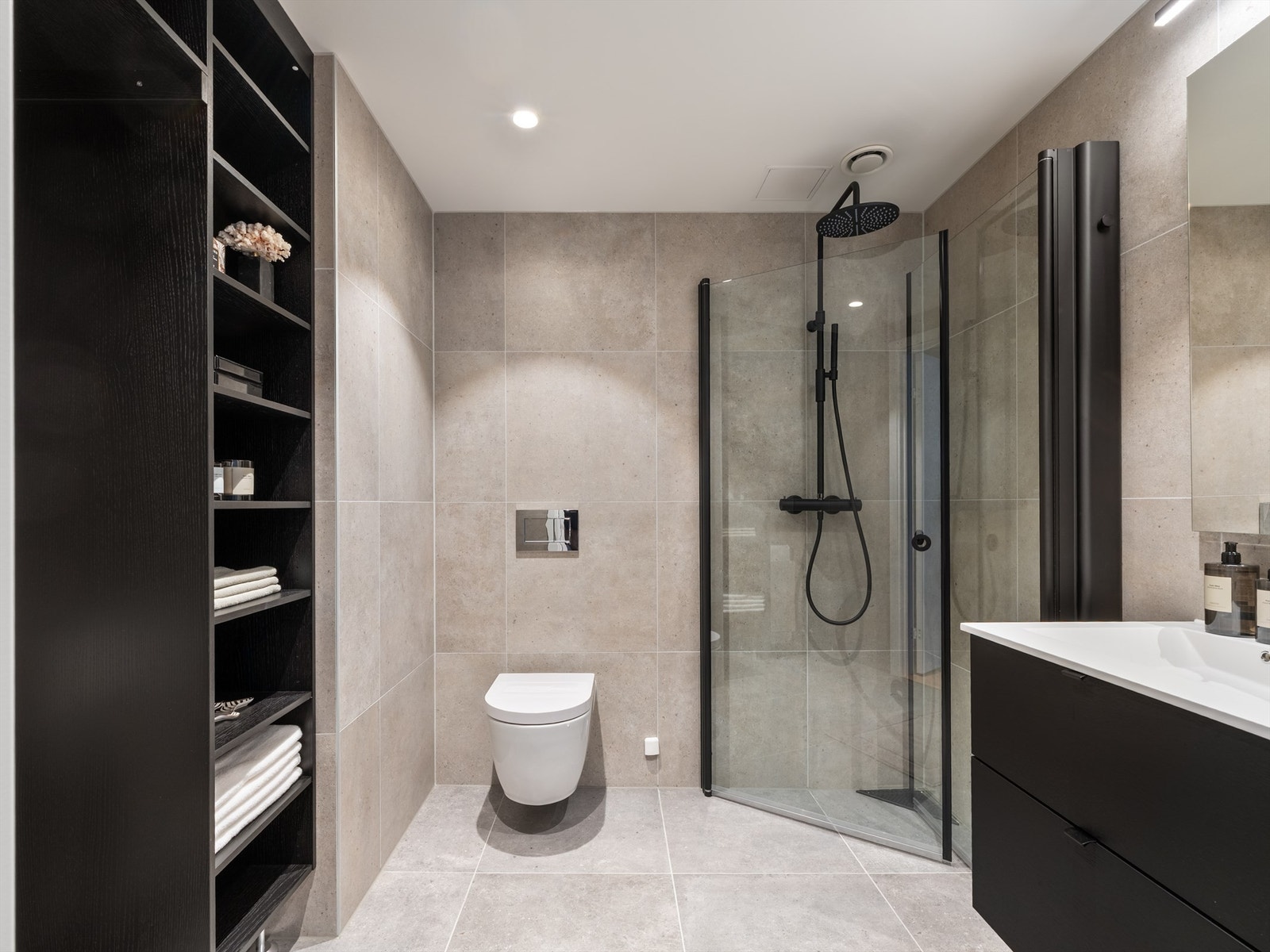 Moderne flislagt bad med skap, wc, dusjhjørne, servant med speil og skapplass. Det er også opplegg for vaskemaskin. Galleribilde