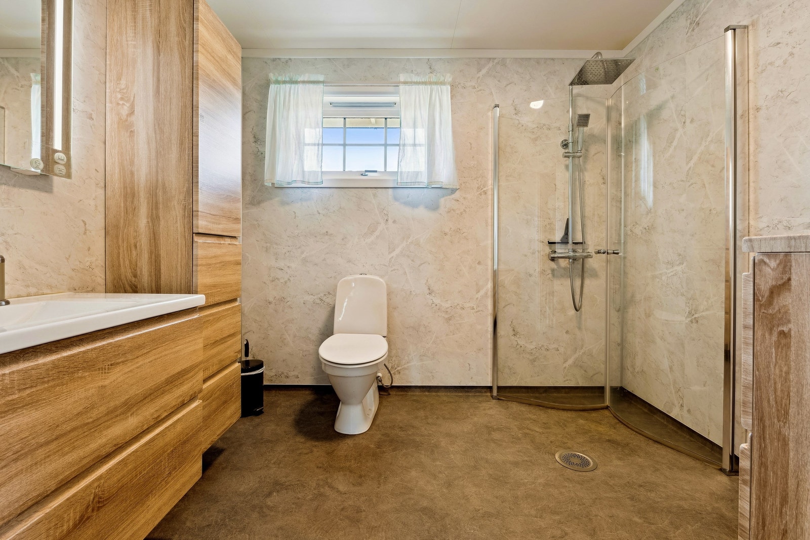 Innredning med servantskap med glatte fronter, speil med belysning, høyskap samt dusjløsning med glassdører. Galleribilde