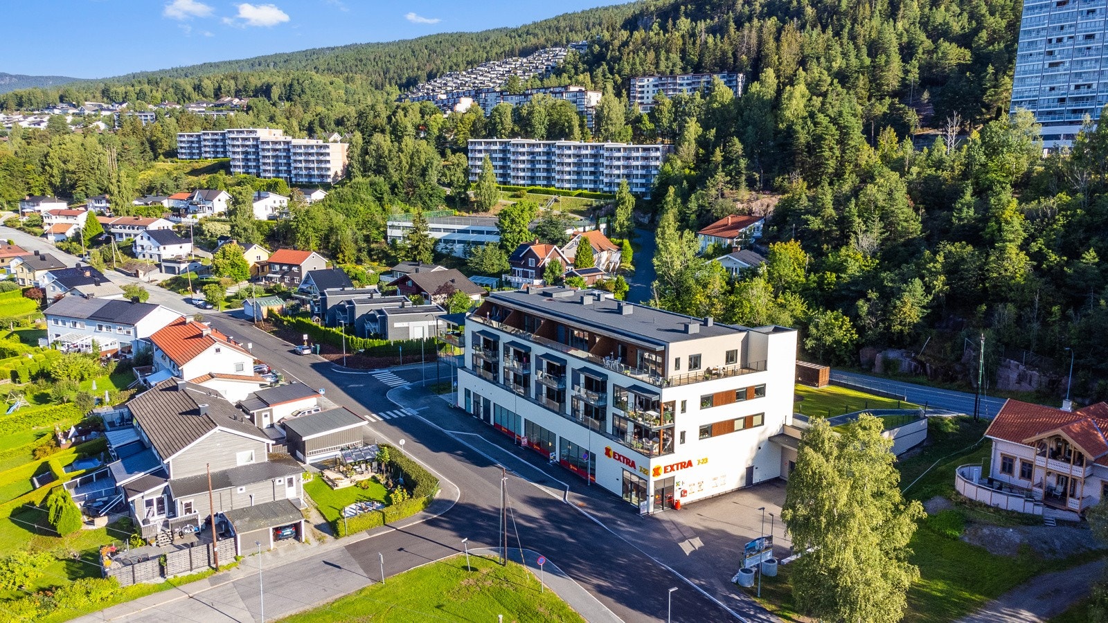 Boligområde med en blanding av eneboliger og leiligheter, omgitt av skog og grønne områder Galleribilde