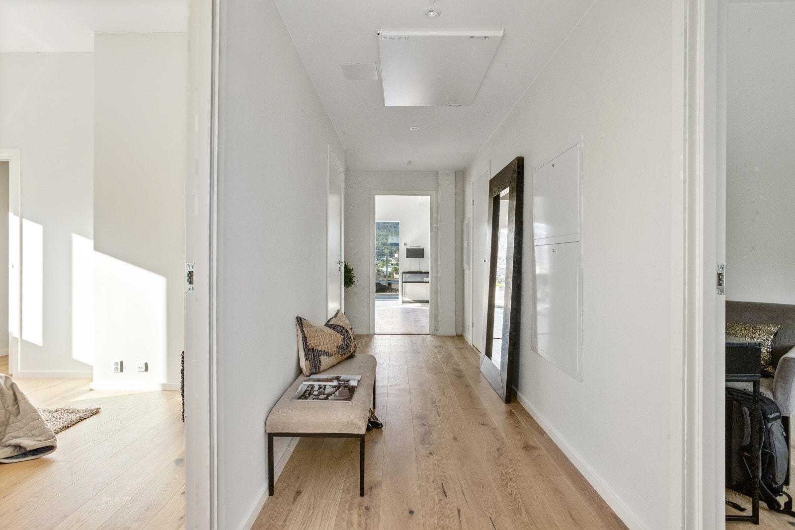 Lys gang med parkettgulv som leder til stue med utsikt. Galleribilde