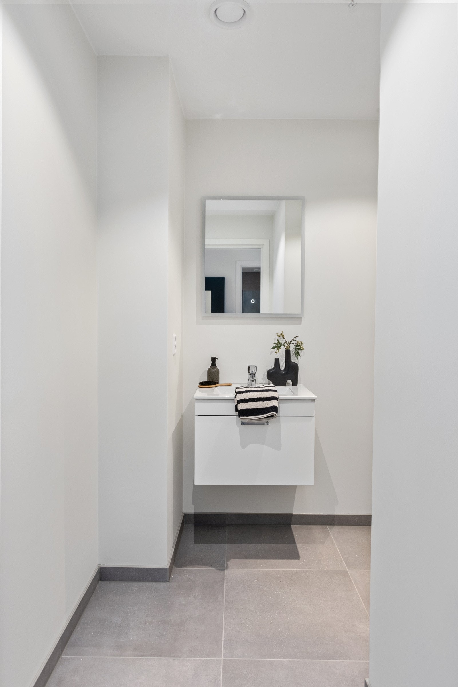 Moderne toalettrom med grå fliser på gulv og hvite vegger. Vegghengt servantskap og speil. Galleribilde