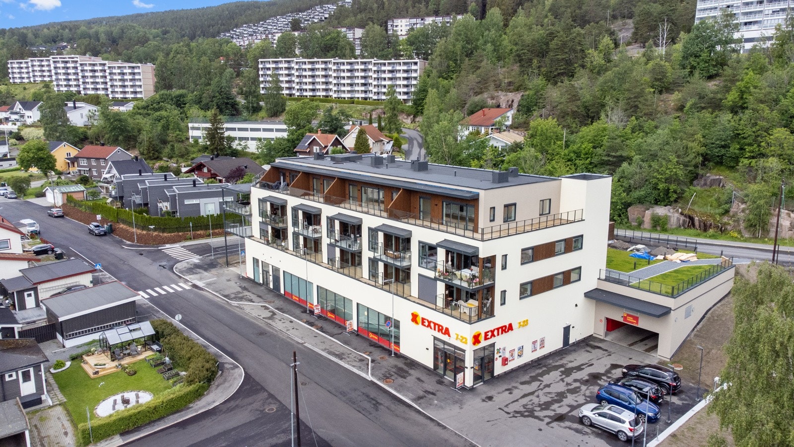 Moderne leilighetsbygg med nærbutikk i første etasje, omgitt av grønne omgivelser. Galleribilde