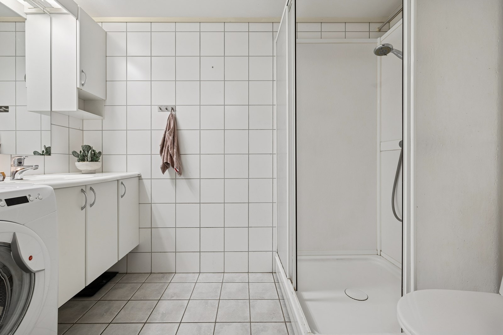 Badet er utstyrt med gulvstående klosett, dusjkabinett med termostatstyrt blandebatteri, baderomsinnredning med glatte fronter og heldekkende servant og speil, samt opplegg for vaskemaskin. Galleribilde