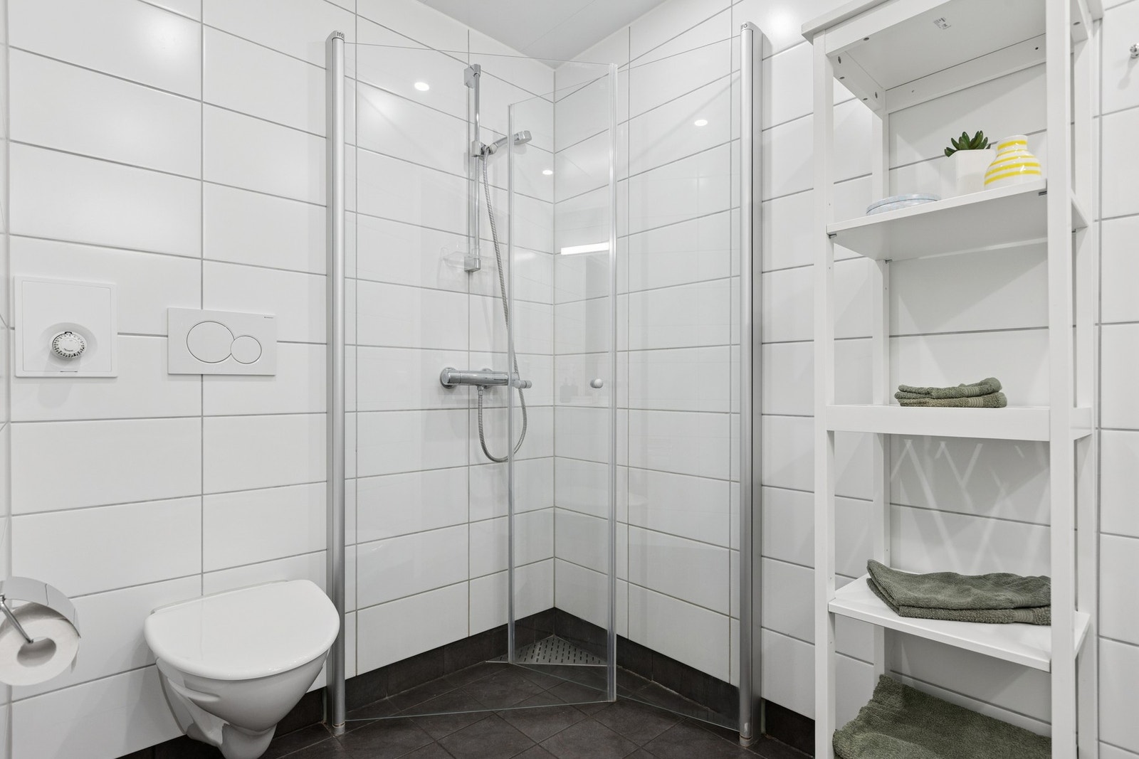 Badet er utstyrt med dusjhjørne, servant med oppbevaring og vegghengt toalett Galleribilde