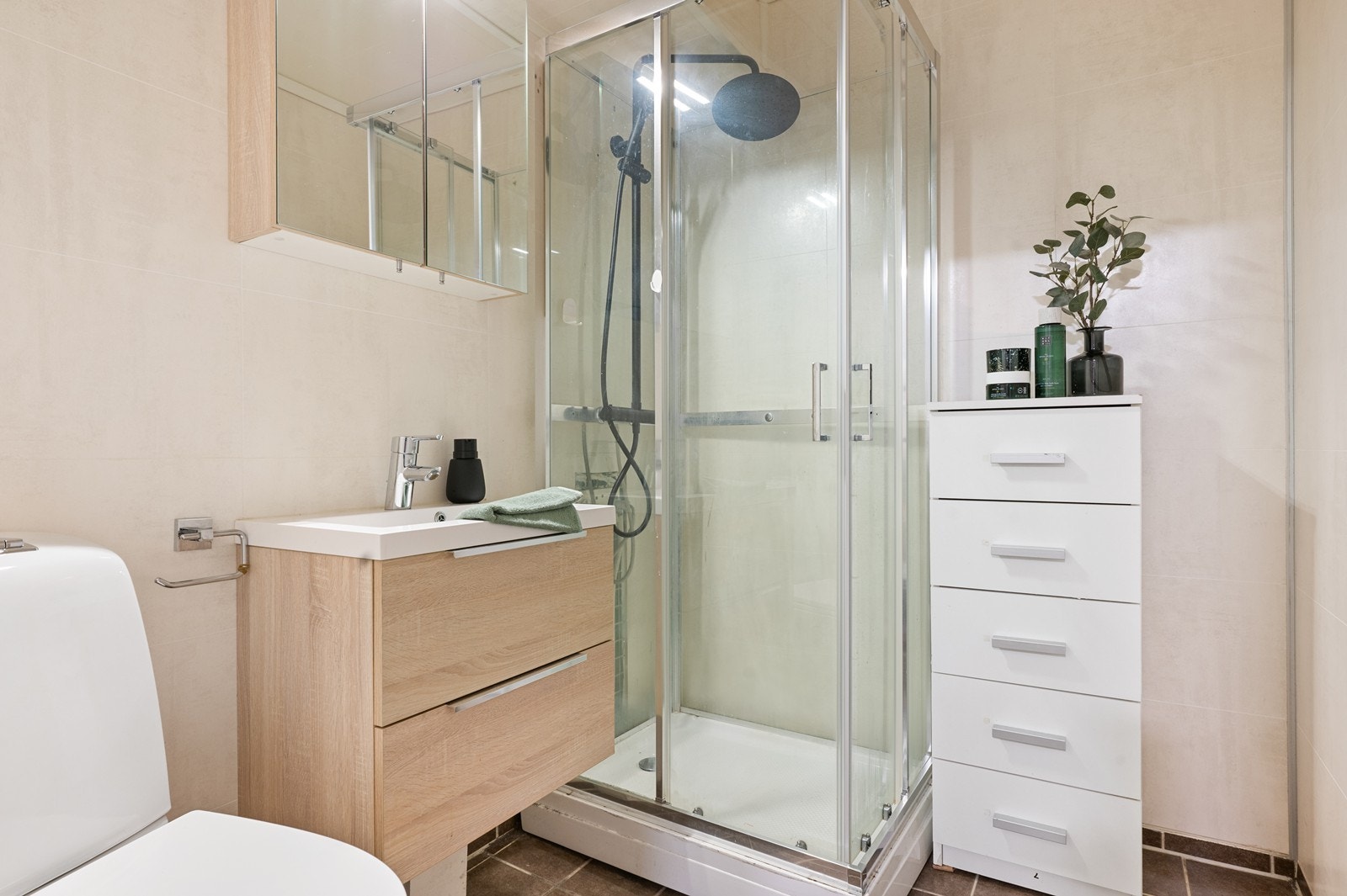 Flislagt bad med sluk fra byggeår der deler er pusset opp med nyere inventar, Inneholder toalett, dusjkabinett og servant med underskap. Galleribilde