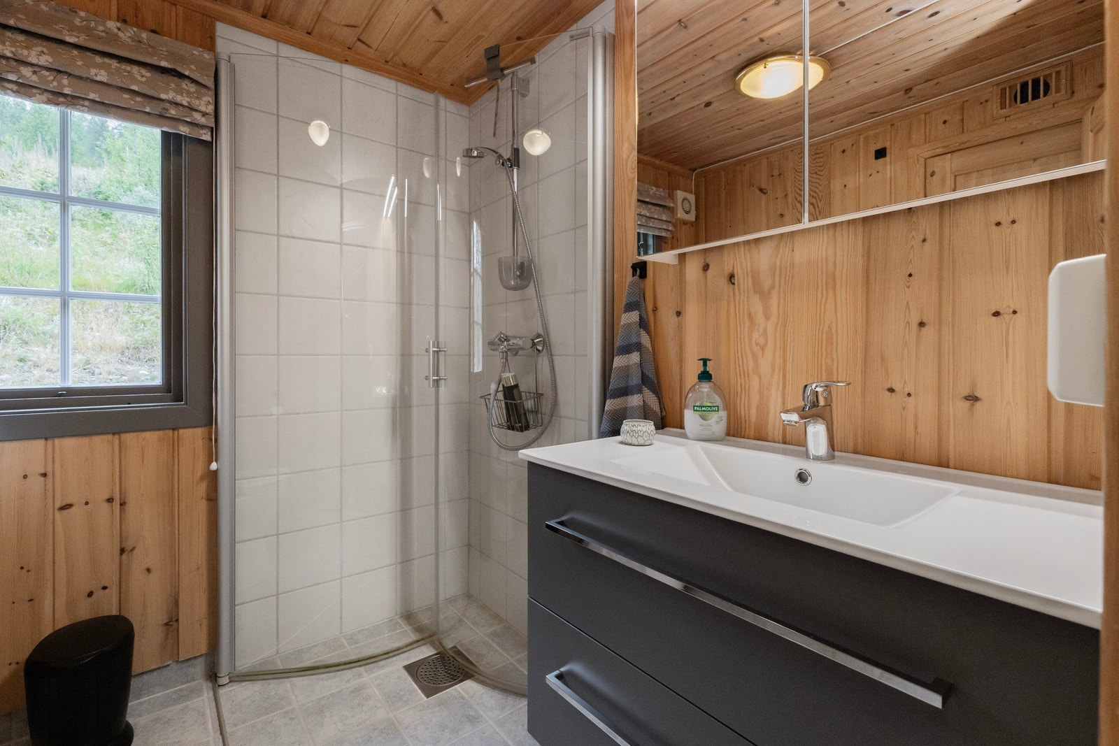 Rommet inkluderer en dusjnisje med glassdører, heldekkende servant på skap og gulvmontert toalett Galleribilde