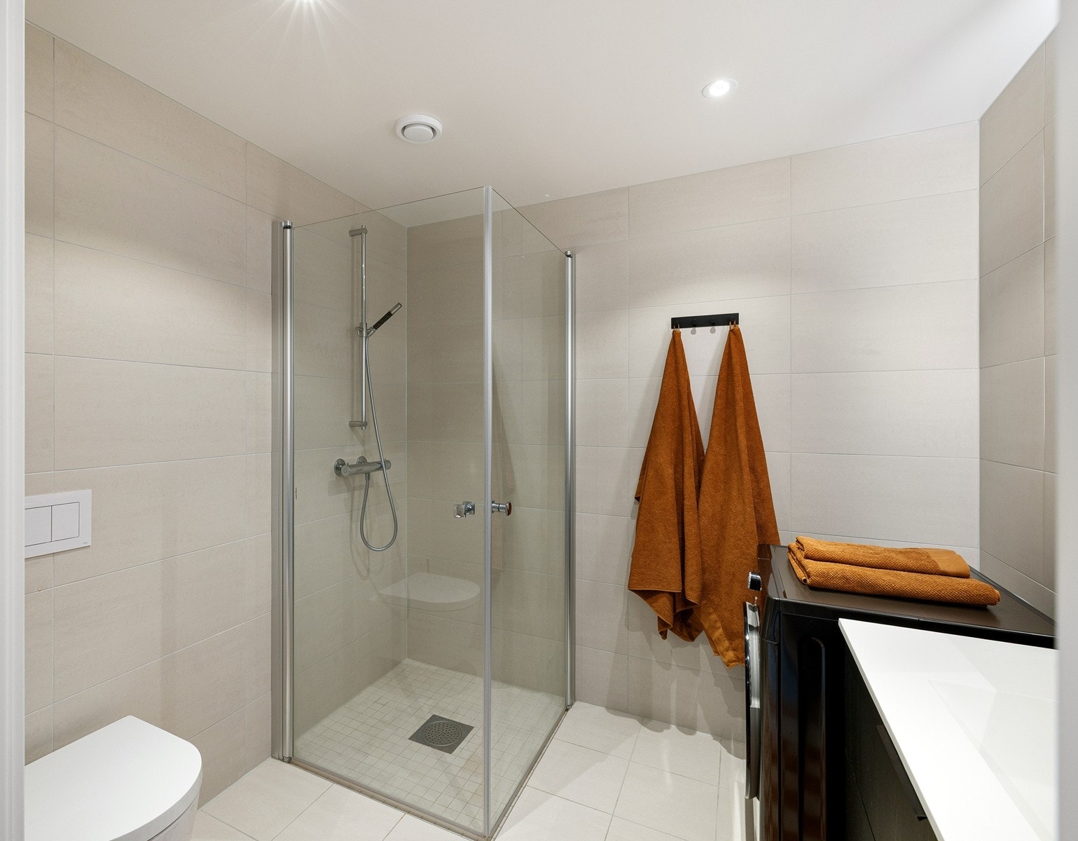 Praktisk dusjhjørne med glassdører, moderne servantinnredning med god oppbevaringsplass og vegghengt toalett. Galleribilde