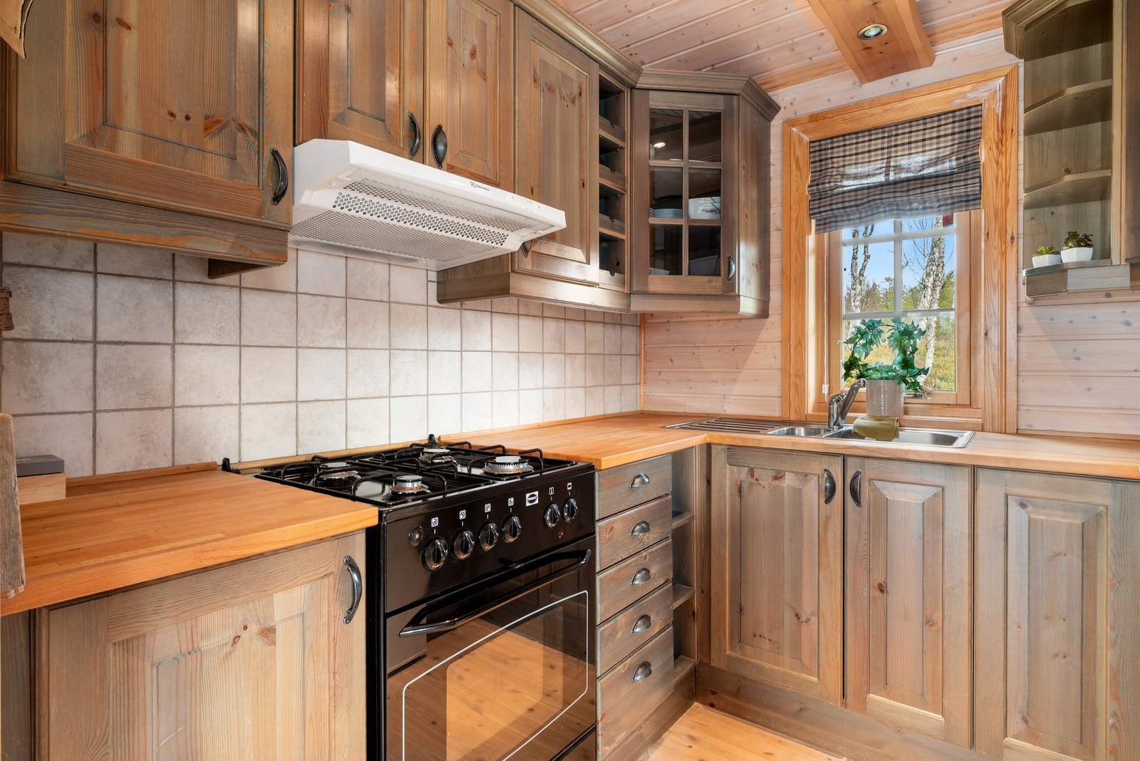 Innredning med mekanisk avtrekksvifte over stekesonen, gasskomfyr og kjøleskap. Galleribilde