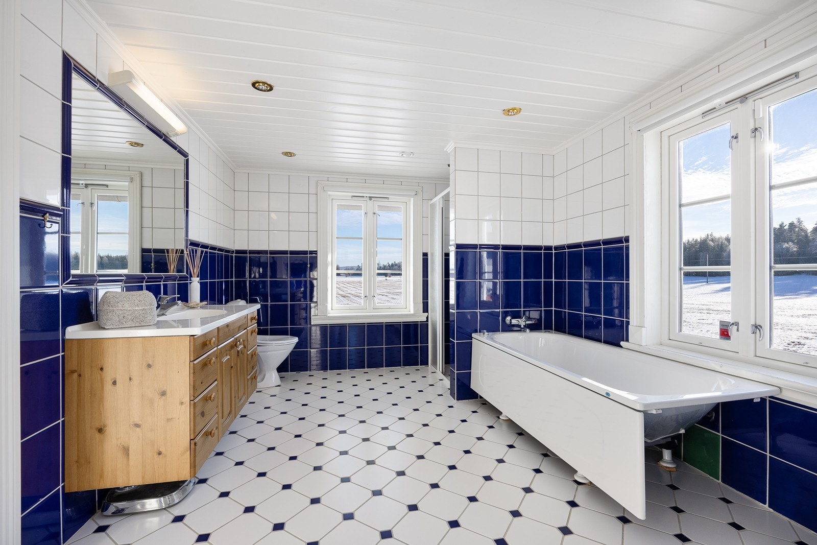 Flsilagt baderom med heldekkende servantplate, et fastfliset speil, toalett, badekar og dusjnisje med glassdør. Galleribilde