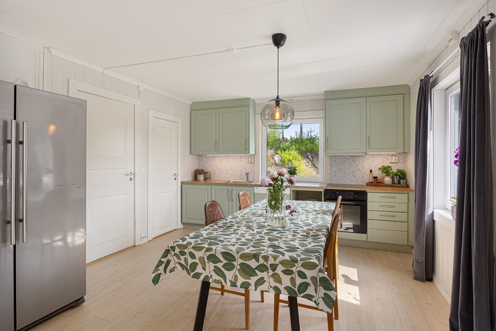 Innredningen har lysegrønne, profilerte fronter, takhøye skap og gyllen laminatbenkeplate med nedfelt kum i stål. Veggen over benken er kledd med lyse plater i flisimitasjon. Galleribilde