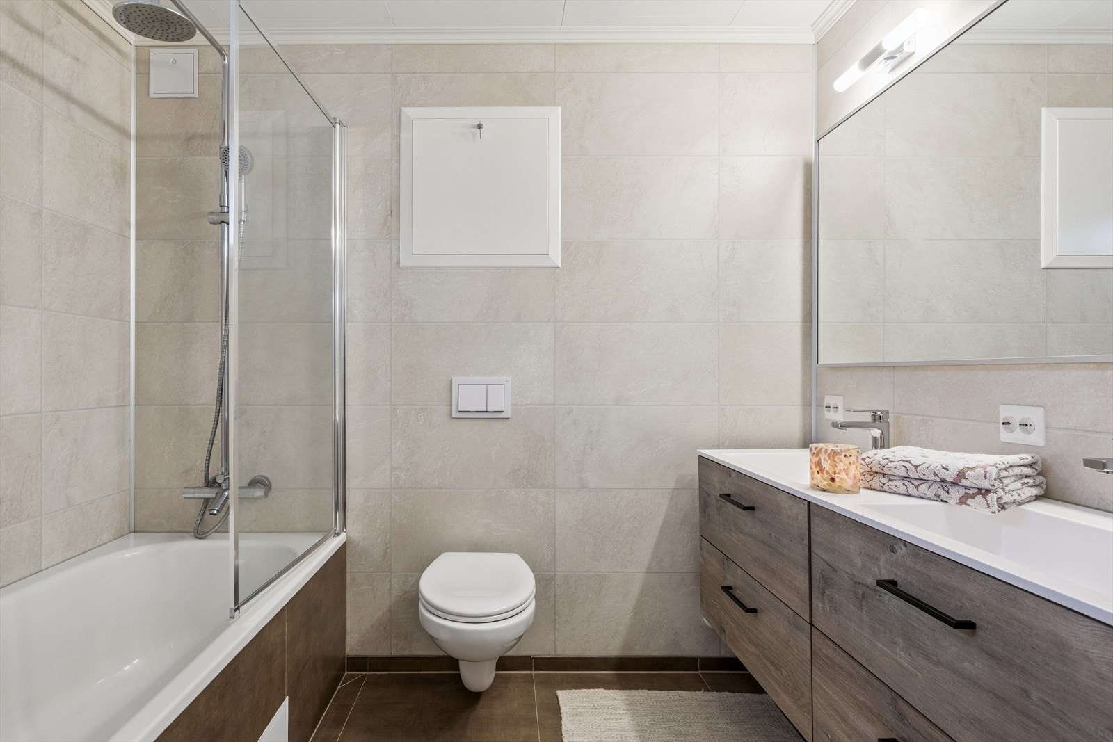 Badet inneholder benk med to vasker, speil m/overlys, toalett og badekar m/dusjgarityr og svingbar dusjvegg i glass. Galleribilde