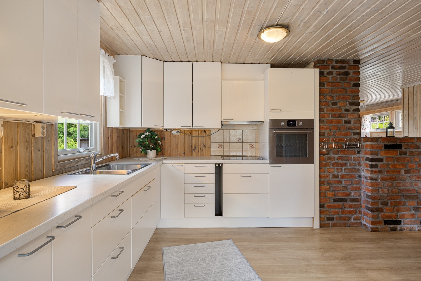 Kjøkkeninnredningen har hvite, glatte fronter og dobbel oppvaskkum nedfelt i en lys benkeplate av laminat. Integrert i innredningen er det platetopp og stekeovn i høyskap. Galleribilde