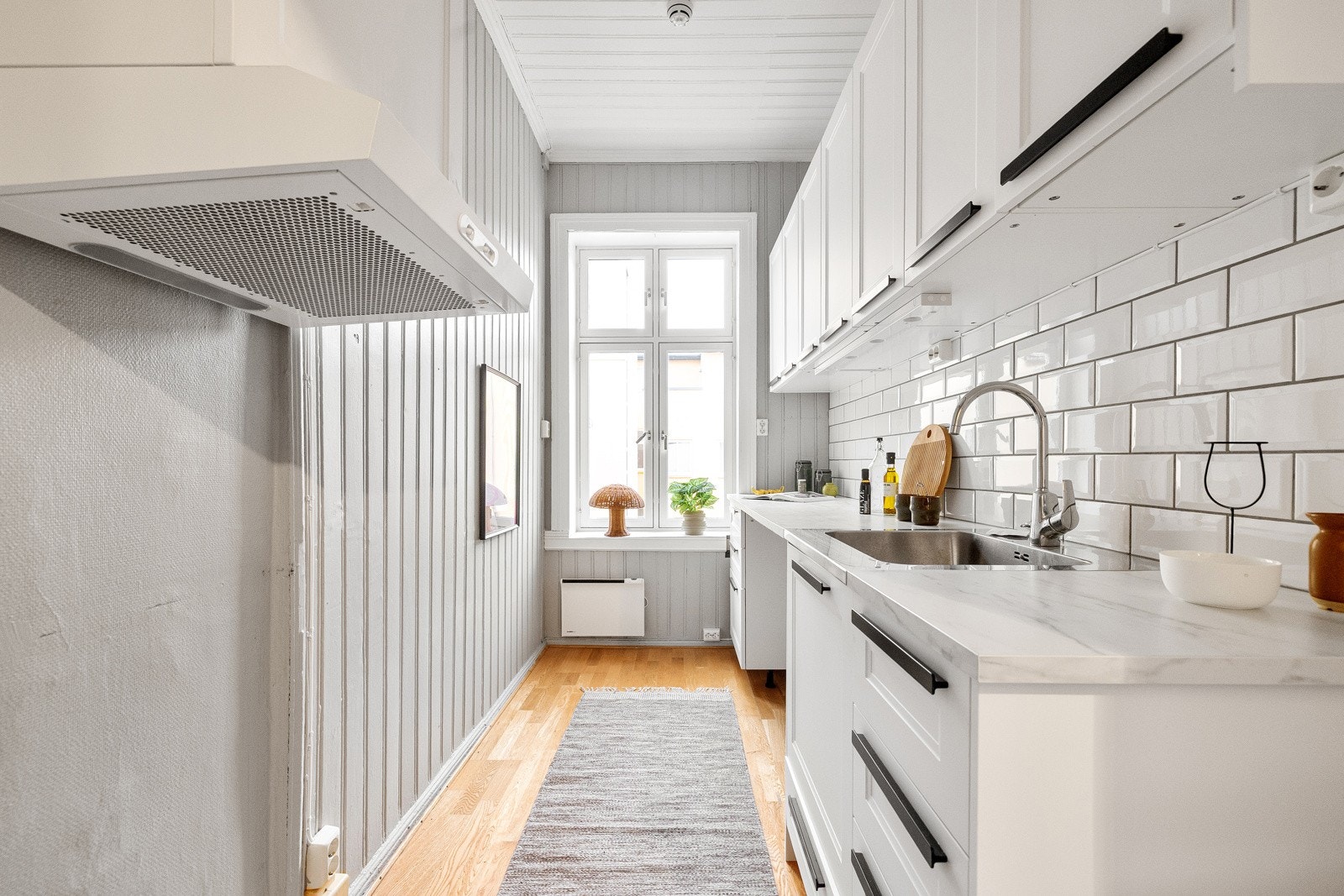 Kjøkkenet har en praktisk utforming med innredning fra IKEA, hvite profilerte fronter og laminert benkeplate med stålkum. Galleribilde