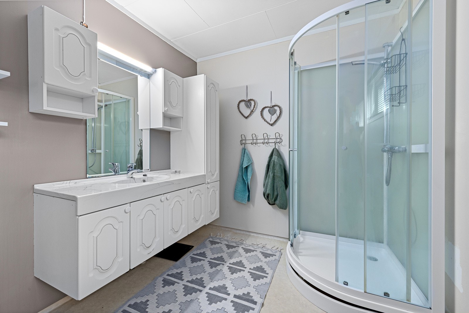 Badet er utstyrt med servantinnredning med heldekkende servanttopp, speil med tilhørende belysning, vegghengte skap, dusjkabinett og toalett. Galleribilde