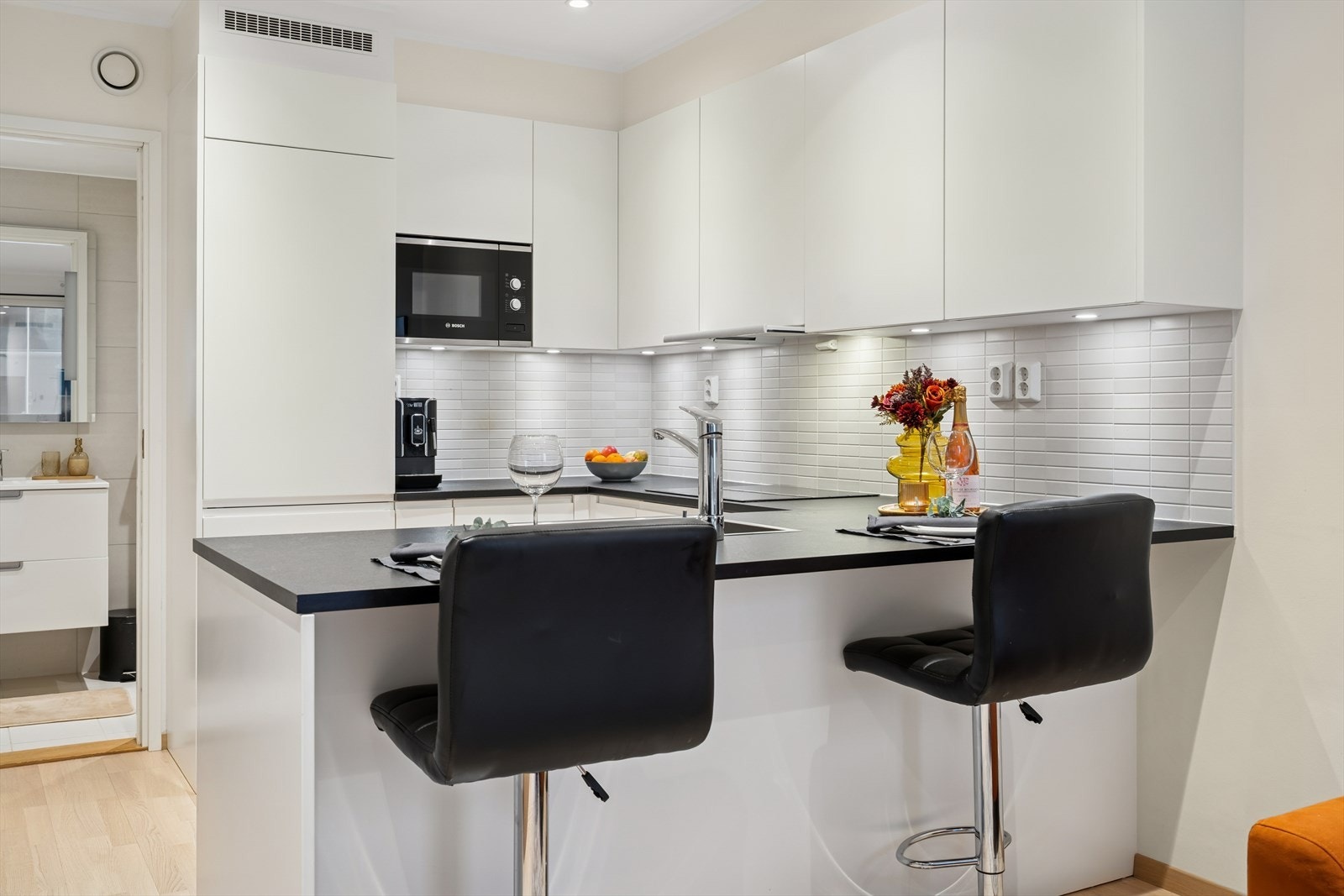 Kjøkkenet har en stilren innredning med hvite glatte fronter, laminert benkeplate med nedfelt kjøkkenvask og fliser på vegg over benk Galleribilde