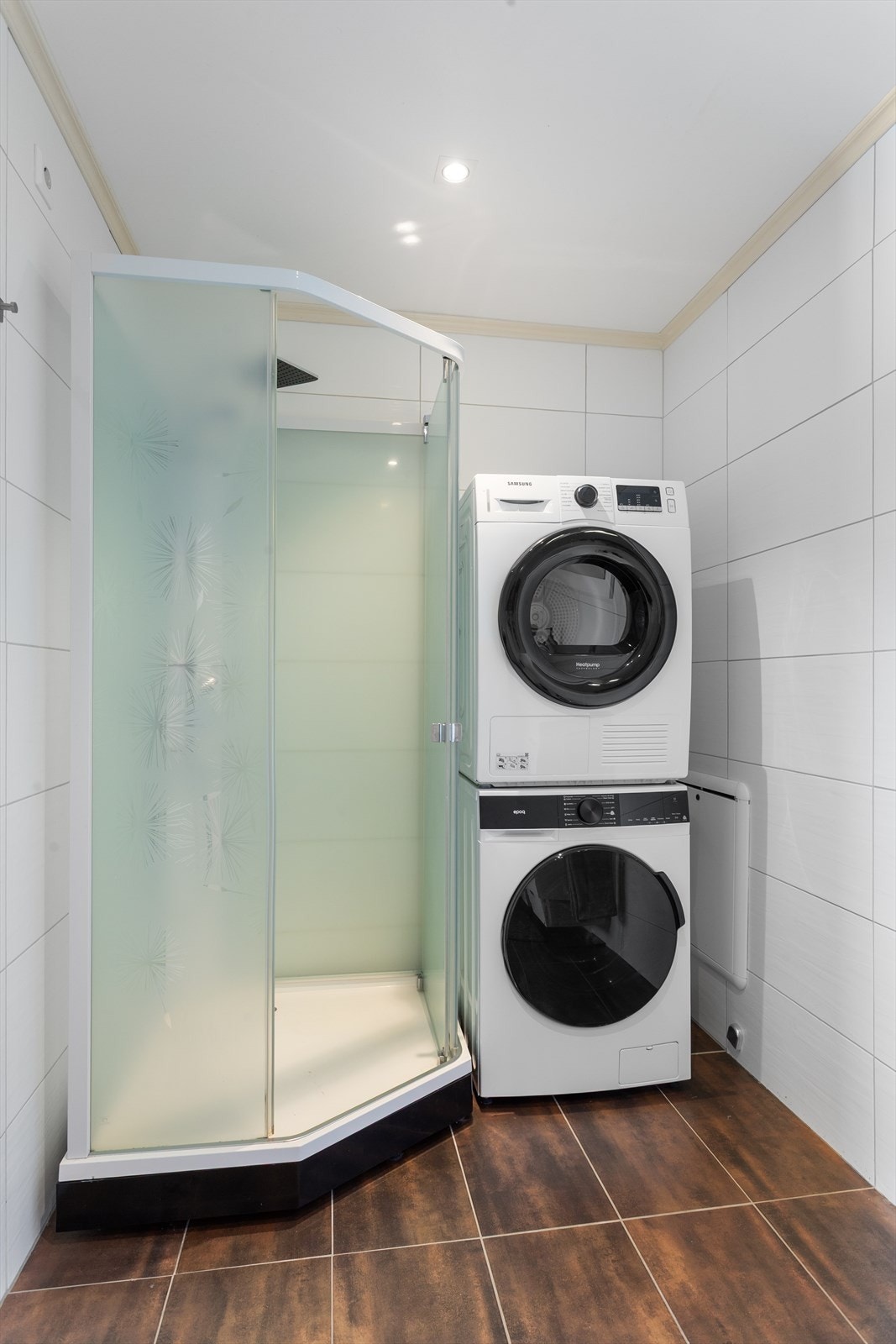 Rommet har en lys innredning med heldekkende servant på skuffer og speil med integrert belysning. I tillegg har badet vegghengt toalett, dusjkabinett og opplegg for vaskemaskin og tørketrommel. Galleribilde