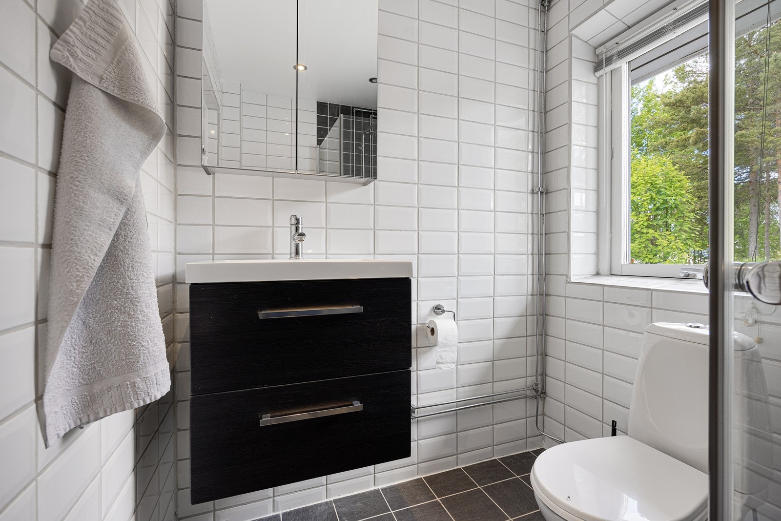 Innredningen består av en heldekkende servant på mørk skuffeseksjon, speilskap, et toalett og et dusjhjørne med regnfallsdusj, hånddusj og innfellbare glassdører. Galleribilde