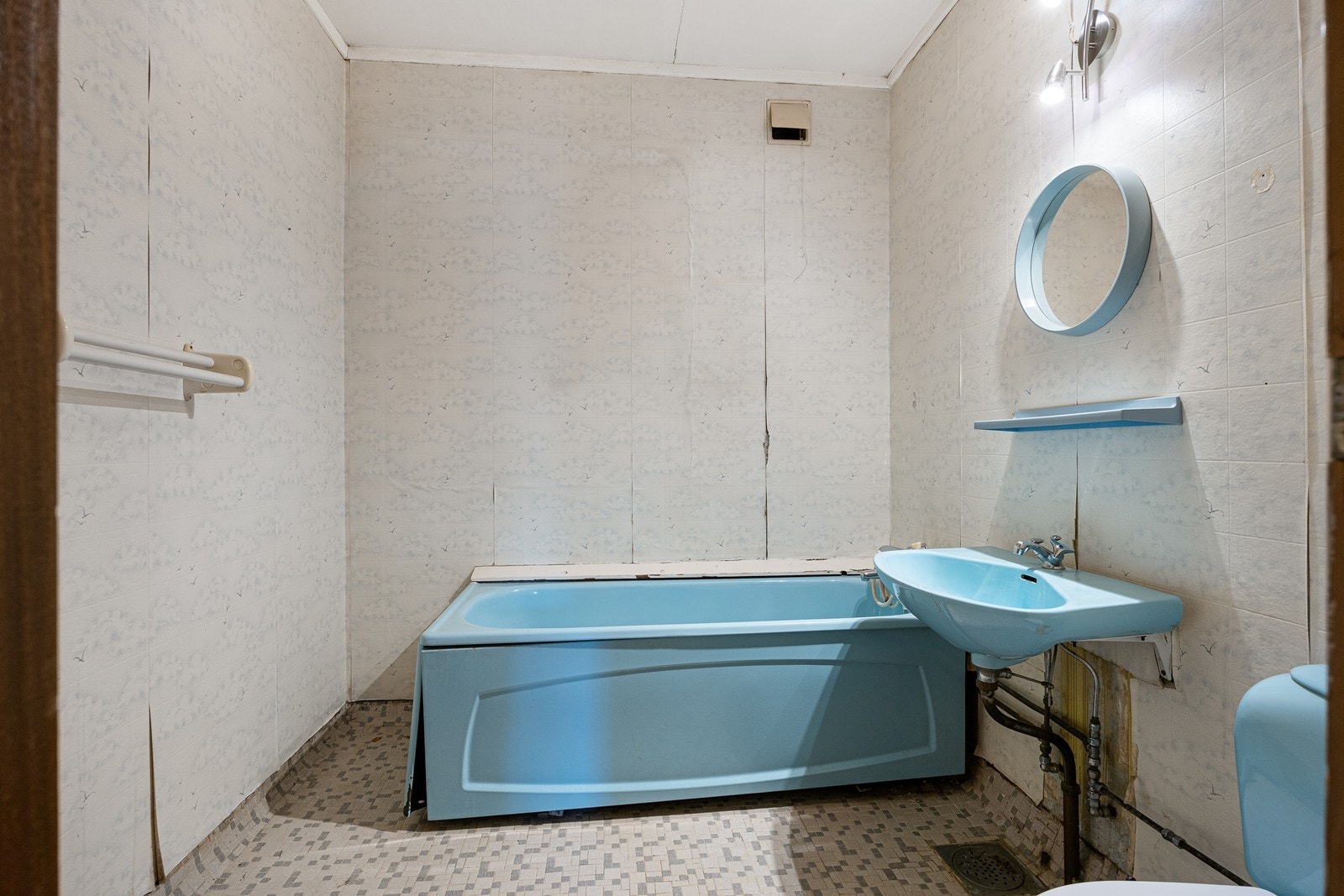 Badet i andre etasje har flislagt gulv, tapet på veggene og oppvarming med stråleovn. Badet er innredet med servant, badekar, toalett, speil og speilhylle i samme turkisfarge. Galleribilde