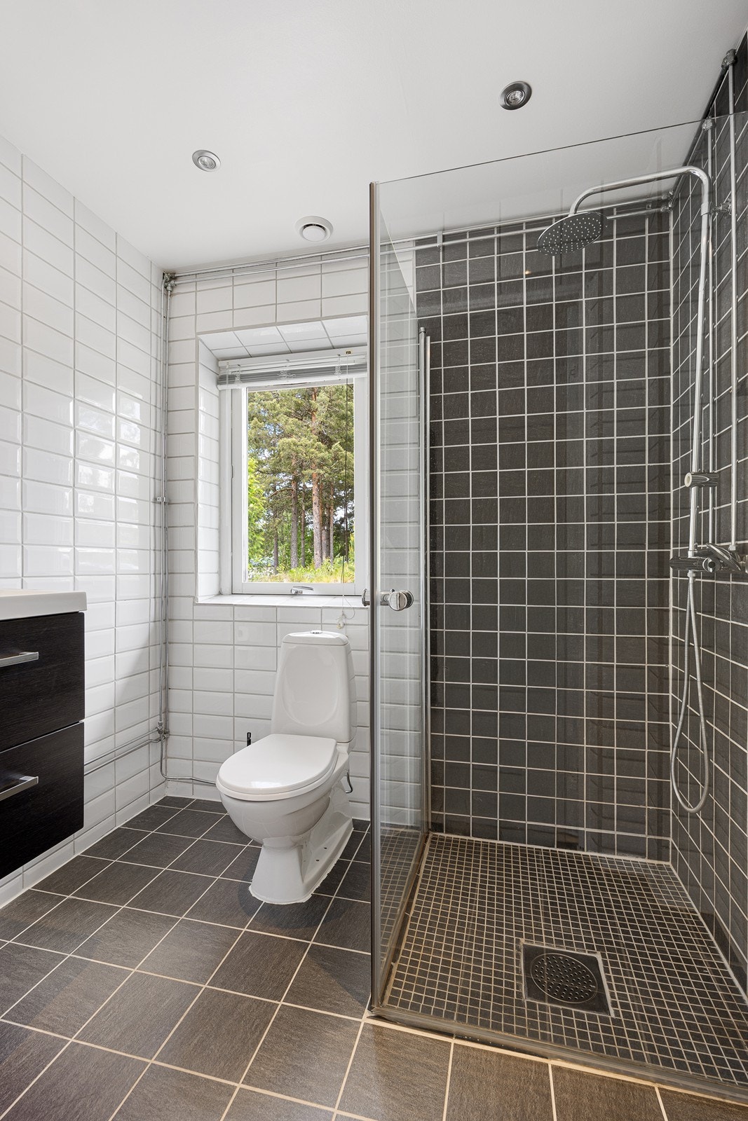 Det ene badet i første etasje ble pent pusset opp i 2014 og fremstår tidsmessig. Rommet er utført med grå fliser på gulvet og i dusjhjørnet, hvite fliser på øvrige vegger, et vindu i endeveggen, downlights i taket og vannbåren gulvvarme. Galleribilde