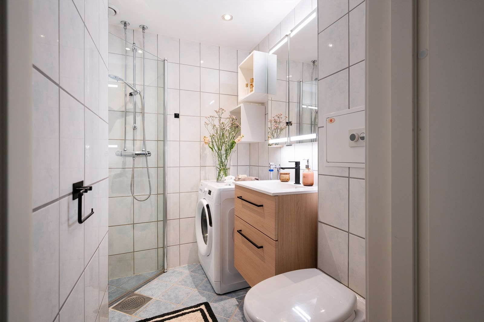 Flislagt bad med dusjnisje og innfellbare dusjdører, servant med ett-greps blandebatteri og vegghengt toalett. Galleribilde