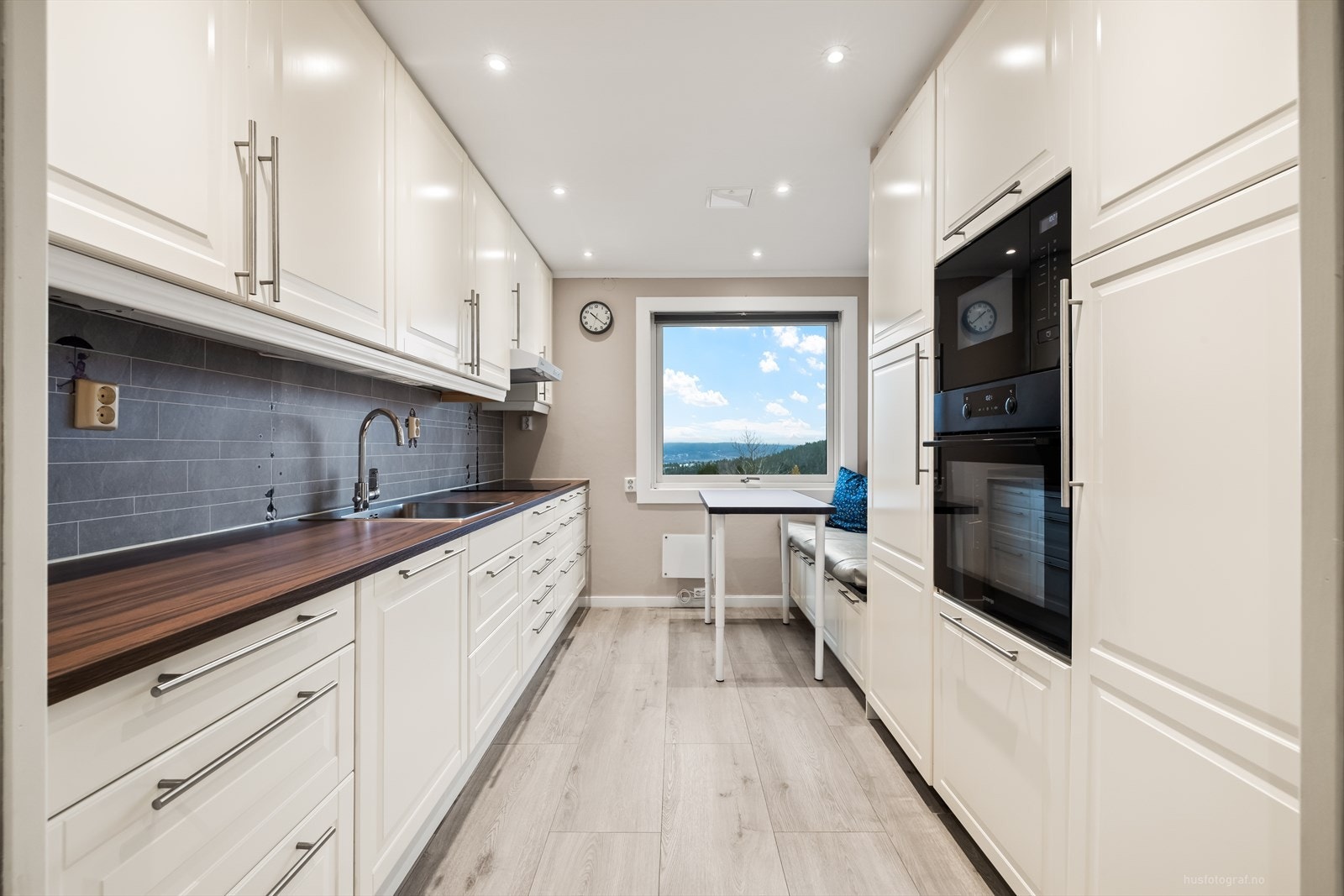 Det er downlights i tak og hvit profilert kjøkkeninnredning. Montert avtrekksvifte over koketopp. God spiseplass ved vindu med plassbygget benk. Galleribilde