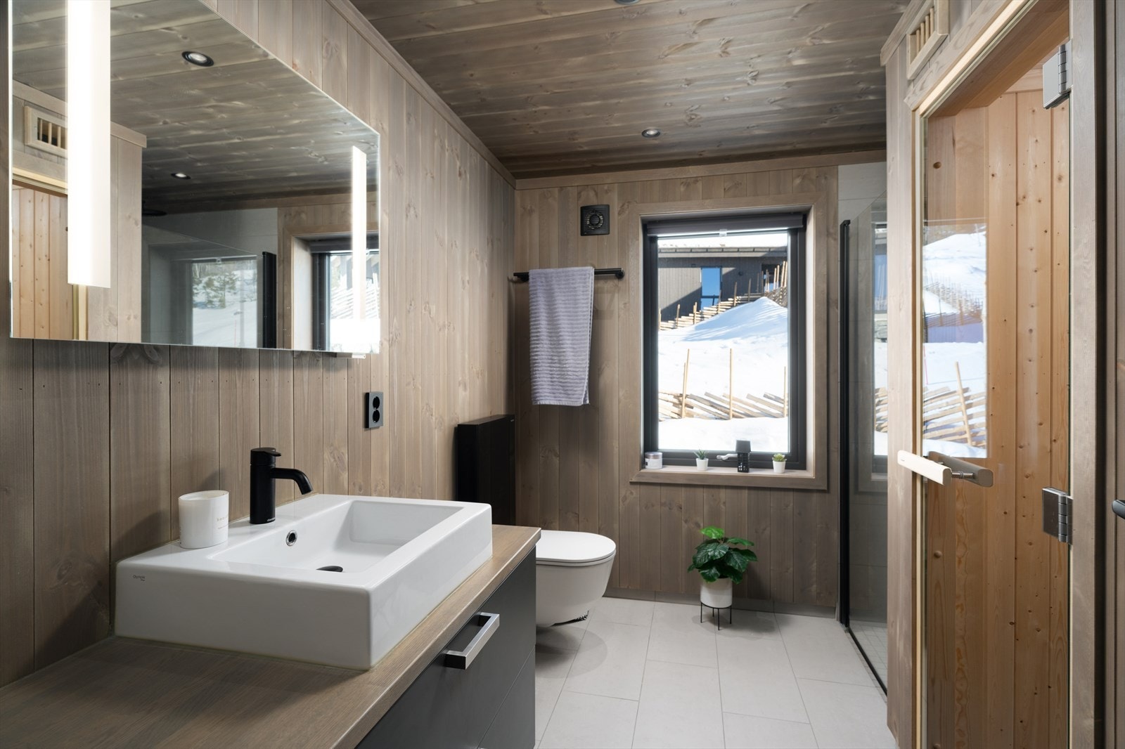 Servantinnredning, veggmontert toalett og dusjnisje med glassdører. Fra badet er det tilgang badstuen. Galleribilde