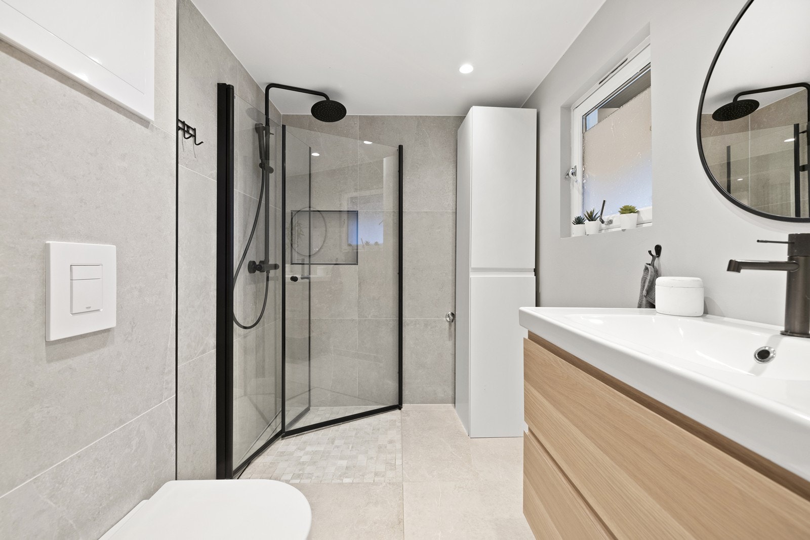 Delikat bad med flislagte gulv og vegger. Badet er utstyrt med vegghengt toalett, servant med skuffer og dusjnisje med innfellbare glassdører. Galleribilde