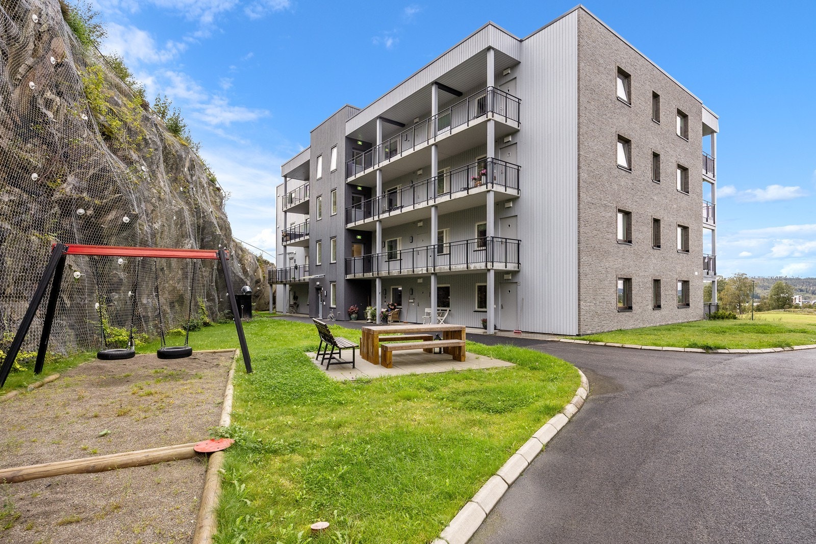 Det er pent opparbeidet rundt bygget med plen, asfalterte veier og planter i skråning. Bak bygget er uterommet godt skjermet av fjell, og her er det et huskestativ til de minste. Galleribilde