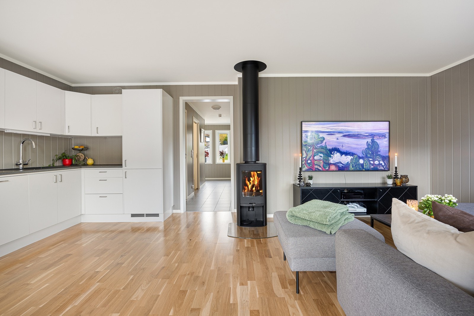 Stue og kjøkken oppleves som et meget hyggelig rom med parkettgulv og veggpanel malt i en harmonisk gråfarge. Galleribilde