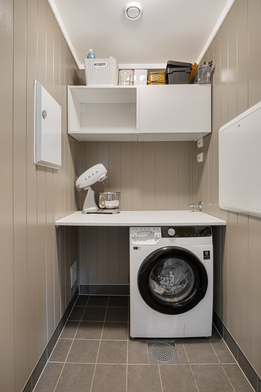 Vaskerommet ligger vegg-i-vegg med badet og er et praktisk rom med flislagt gulv, malte veggplater og avtrekk via balansert ventilasjon. Rommet er opprinnelig byggemeldt som bod. Galleribilde