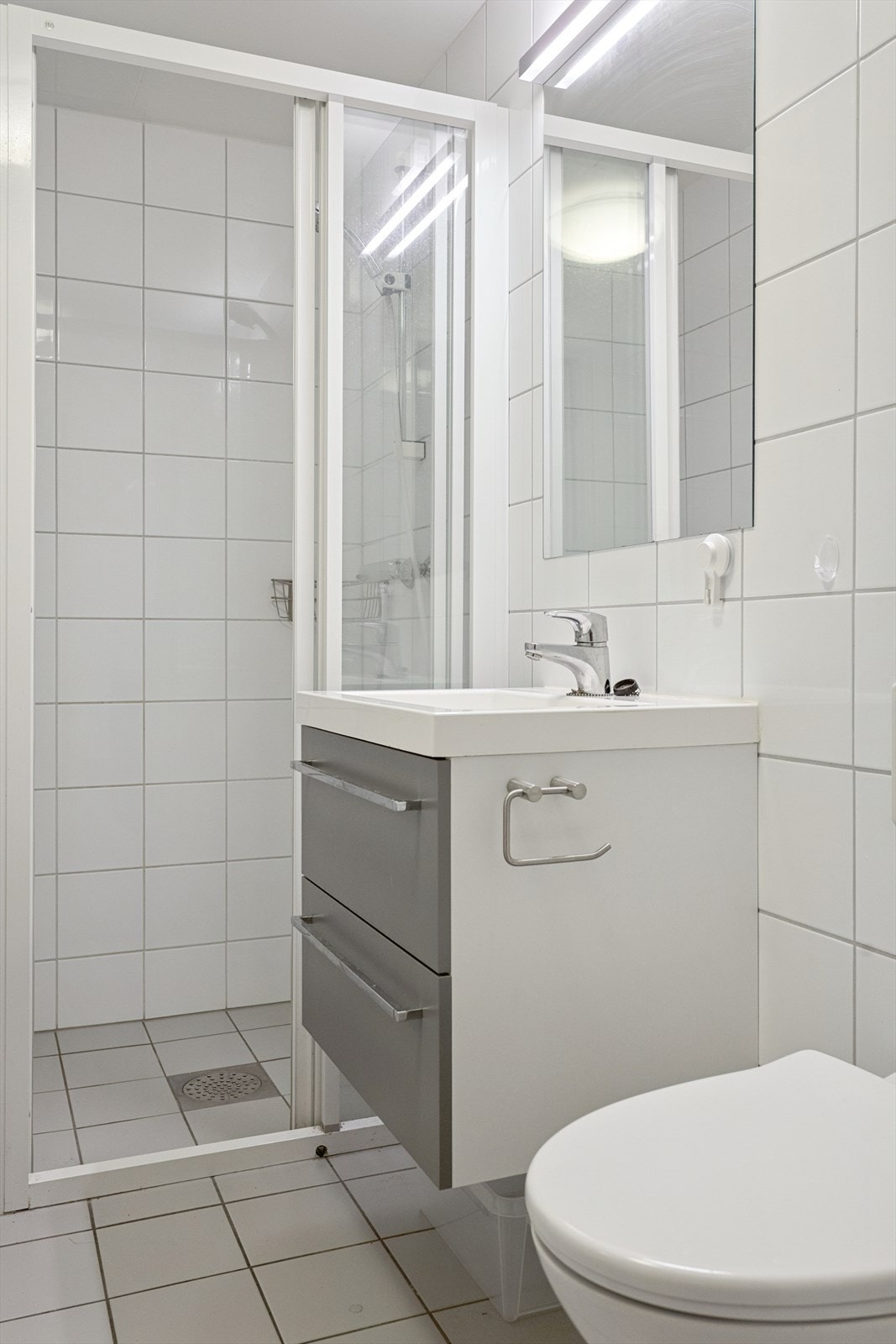 Baderommet har vegghengt toalett, dusjvegger av glass, opplegg for vaskemaskin samt innredning med servant. Galleribilde