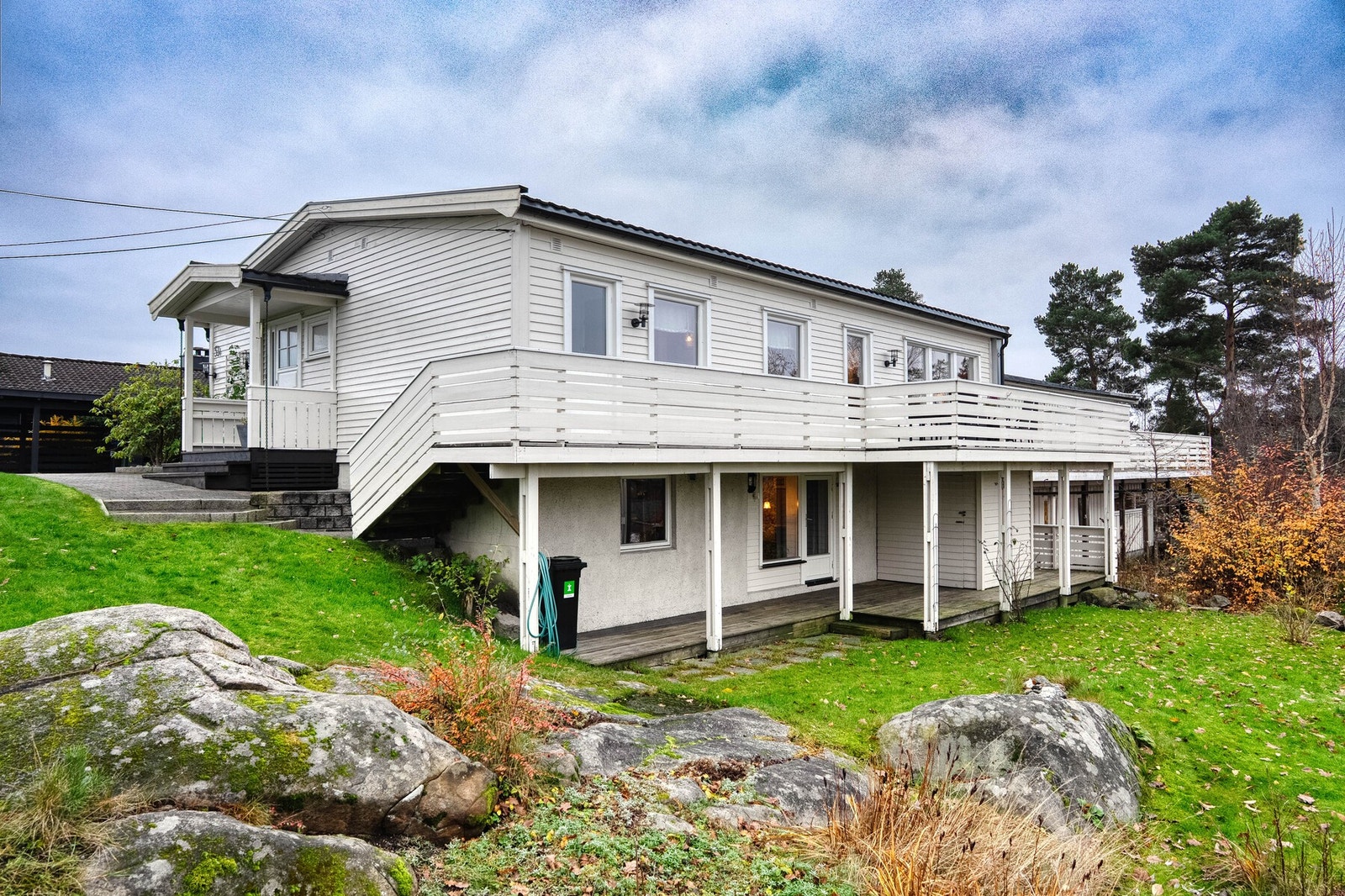 Tomten er pent opparbeidet med gressplen, beplantning, carport og asfalterte biloppstillingsplasser. Galleribilde