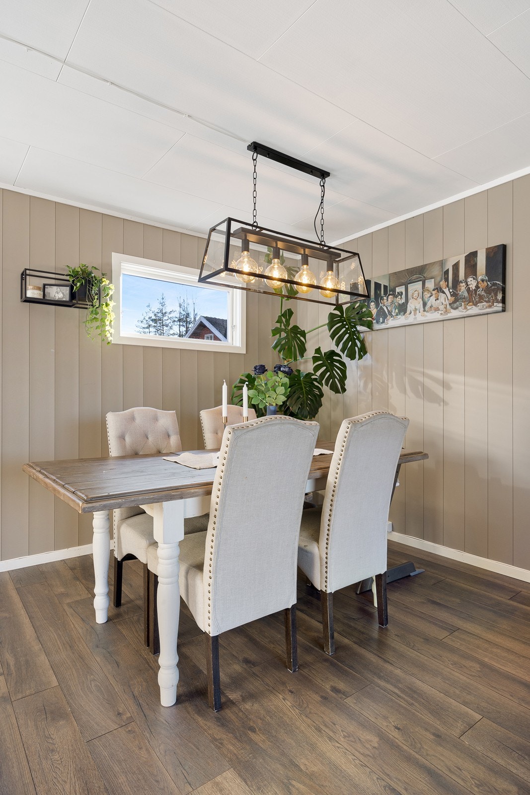 Stuen har enstavs laminatgulv, beigemalte panelvegger, hvite takessplater og pipeløp kledd i tegl. Galleribilde