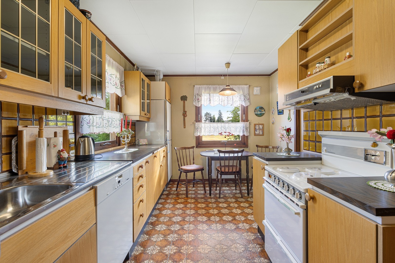 Kjøkkeninnredningen har glatte, finerte fronter, vitrineskap og benkeplate av laminat. Over benken er det keramiske fliser. Det er opplegg for oppvaskmaskin og avsatt plass til komfyr. Galleribilde