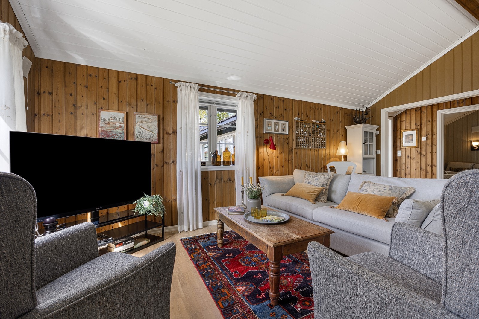 Stuen har mørkbeiset panel på veggene, hvitmalt panel i himlingen og trestavs parkett på gulv med luftbåren gulvvarme. Galleribilde