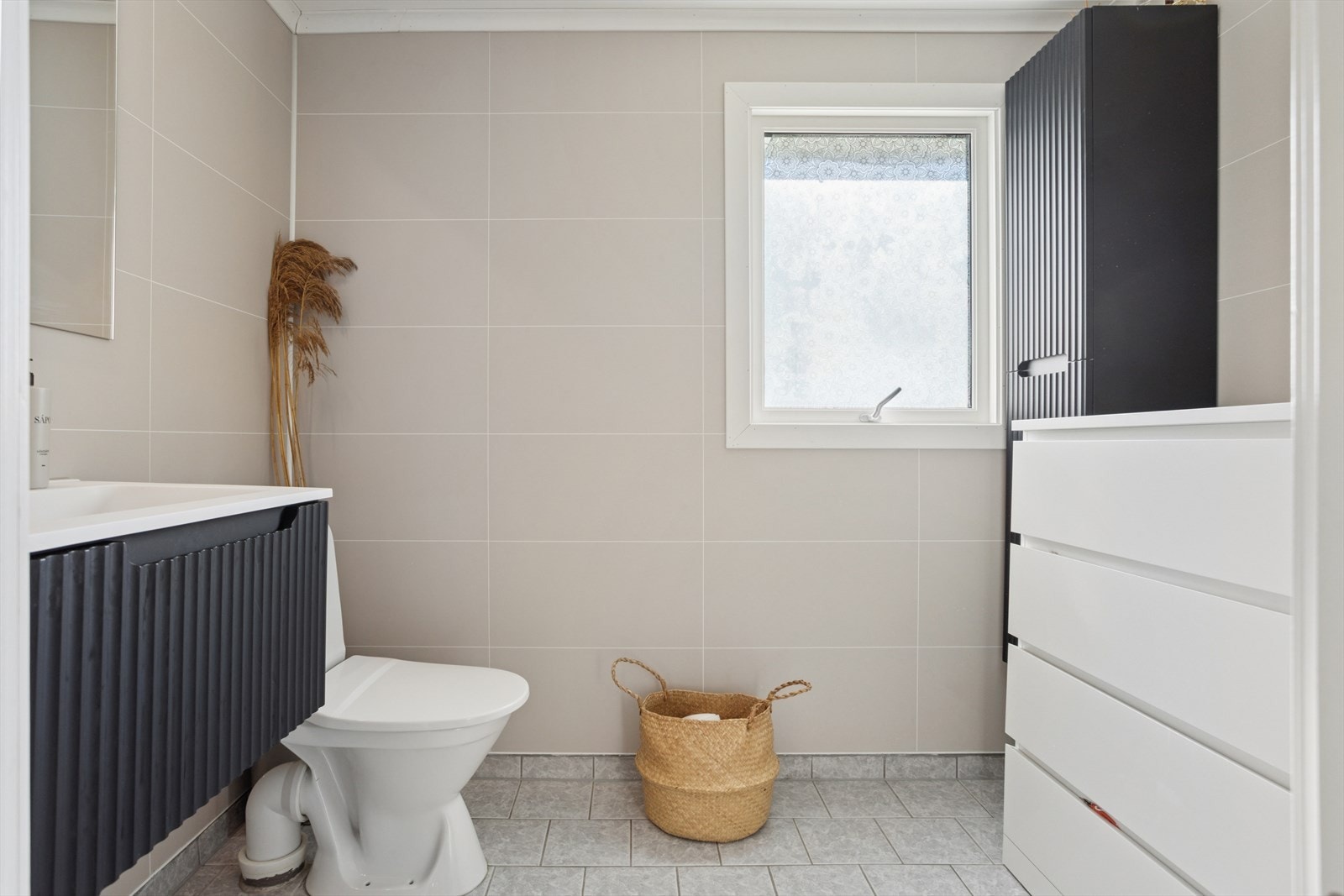 Baderom med keramiske fliser på gulv, baderomsplater på vegger og malt panel i himling.
Det er avtrekksventil i himling og varmekabler i gulv. Galleribilde