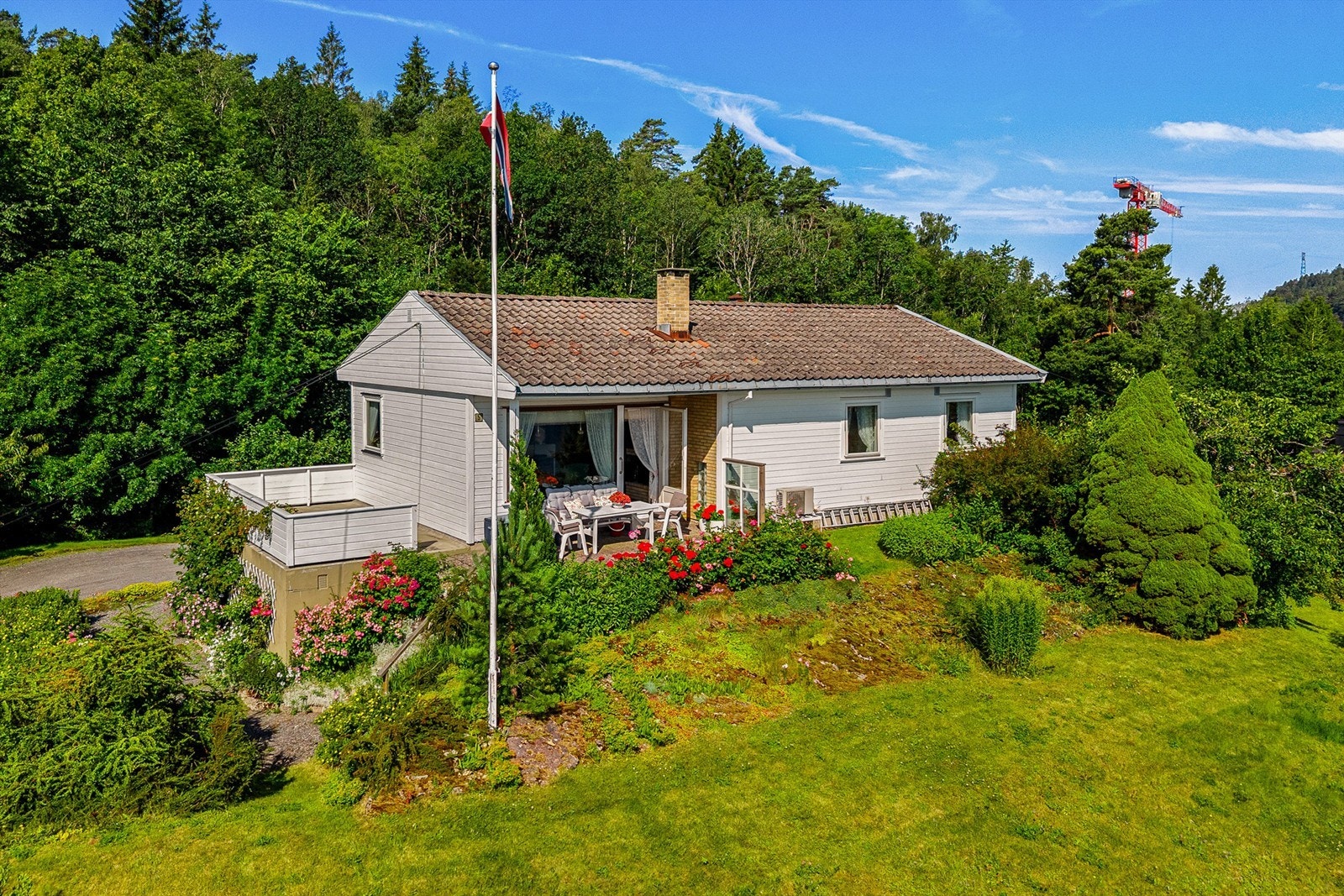 Eneboligen ligger lunt til, omkranset av grønt og blomstrende hage. Galleribilde