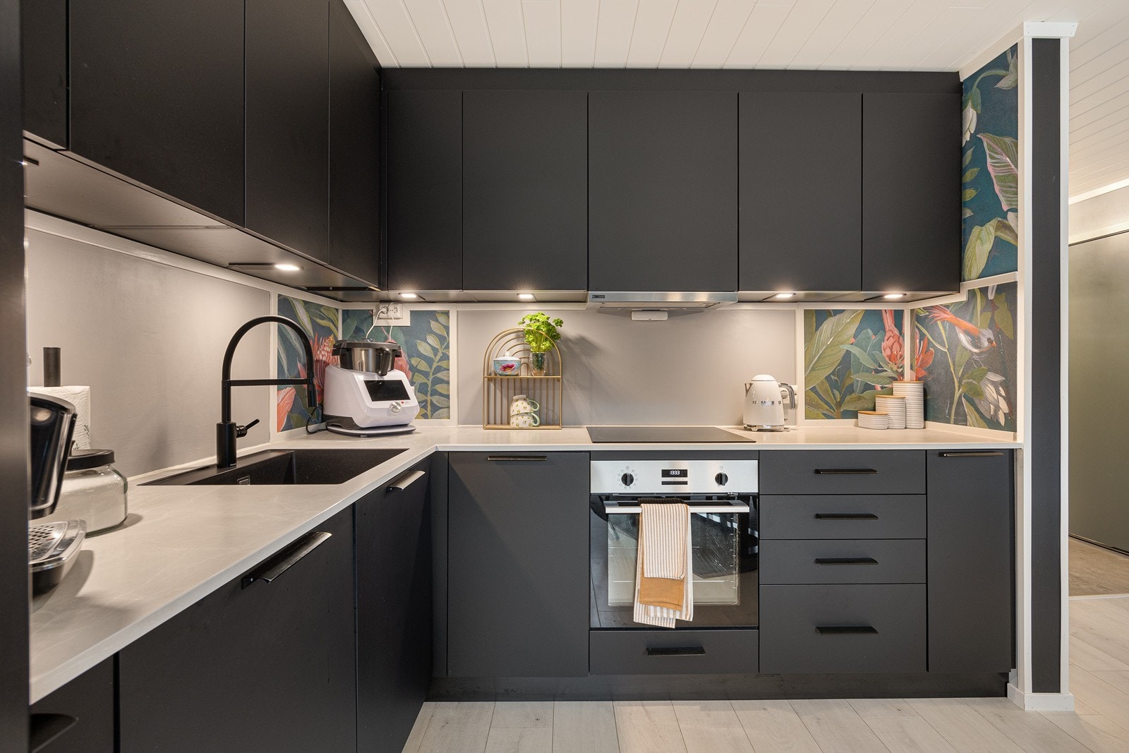 Spotter er montert over benken, og deler av veggen har den samme tapeten som stuen. Integrert i innredningen finner man stekeovn, induksjonstopp og oppvaskmaskin. Galleribilde