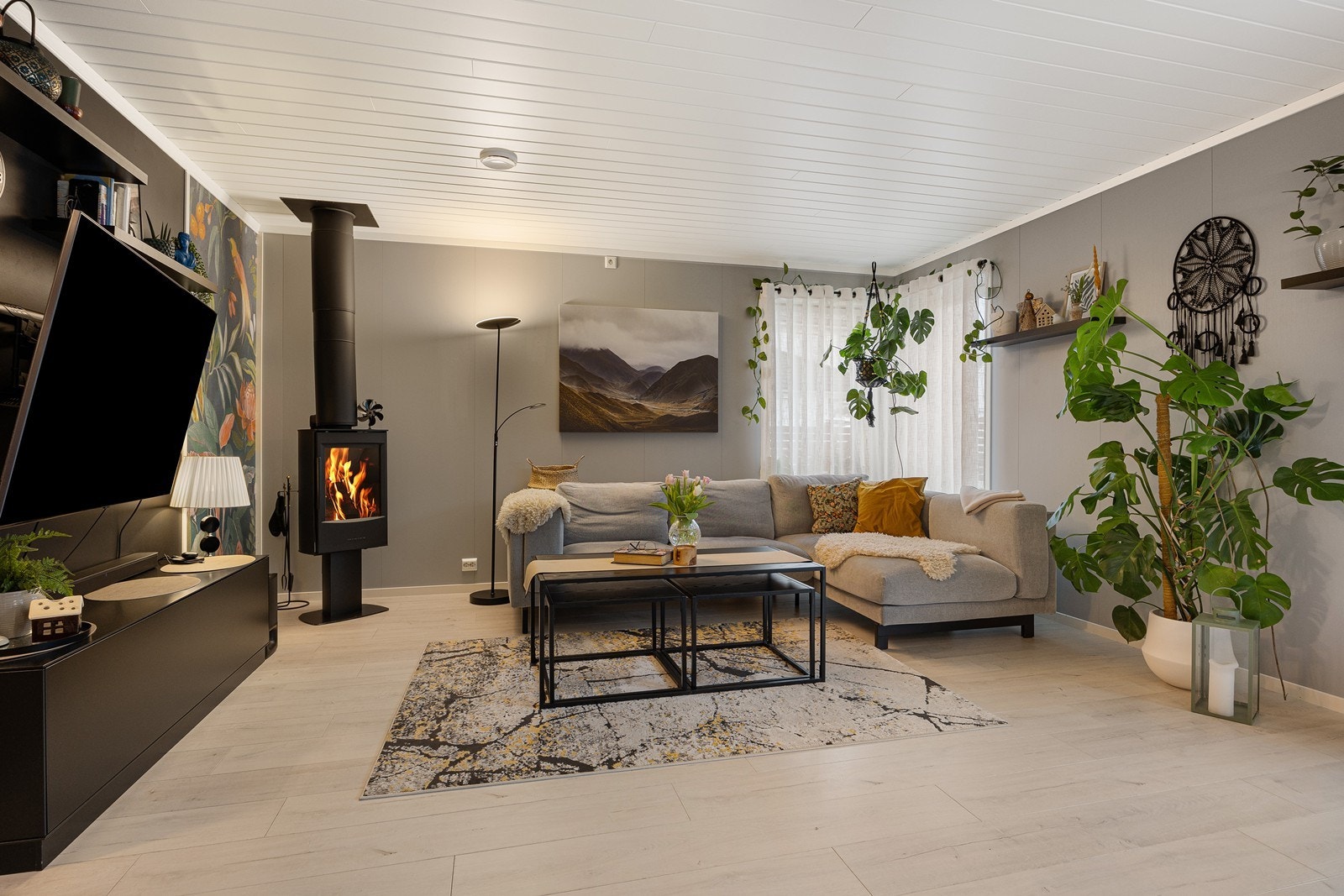 Parkettgulvet fra entreen fortsetter inn i stuen for et helhetlig uttrykk. Veggene er malt i ulike grånyanser, og innslag av en tapet med fugler og blomster gir en fin kontrast. Galleribilde