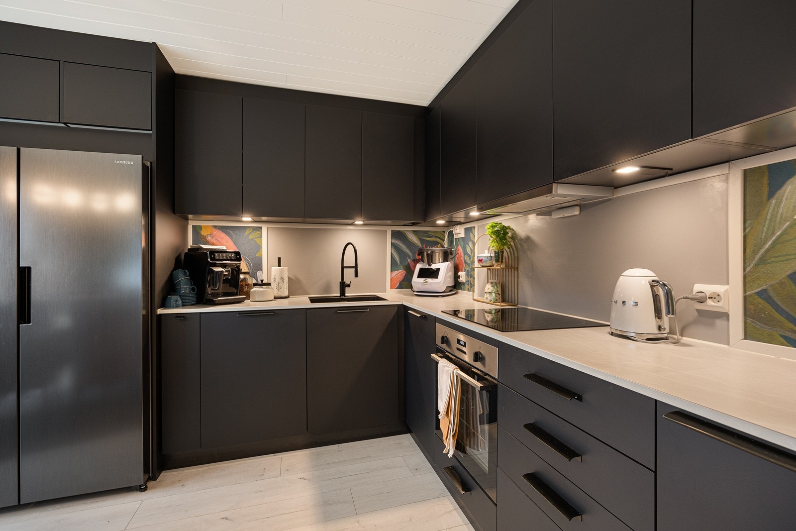 Innredningen har sorte, glatte fronter, lekkert vitrineskap, et hendig høyskap og sort oppvaskkum nedfelt i en laminert benkeplate. Det er nisje for side by side kjøleskap, og over kokesonen er en ventilator med avtrekk etablert. Galleribilde