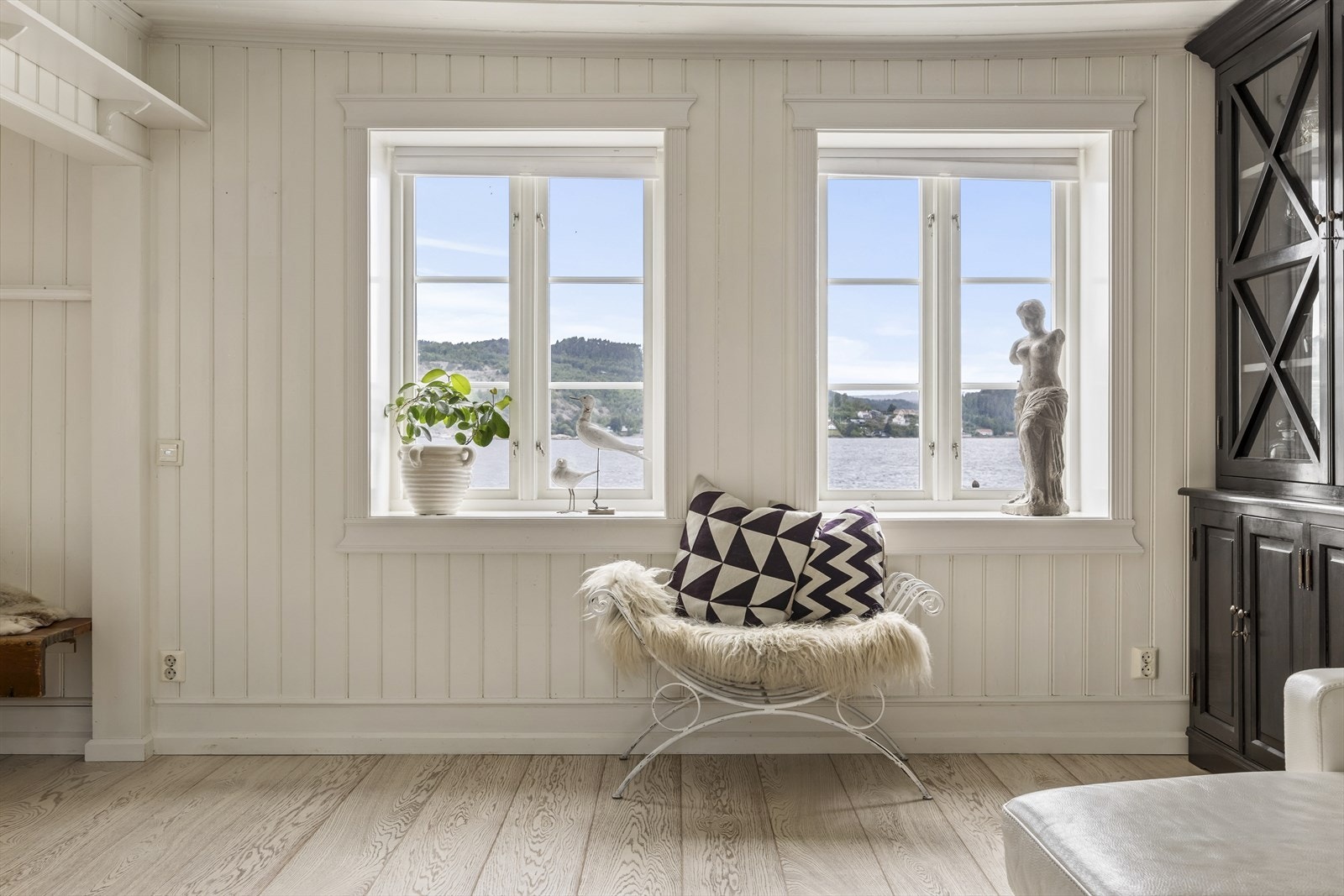 Koselig stue med store vindusflater, parkett på gulvet og malt panel på veggene - perfekt til boligens naturlige sjarm. Galleribilde