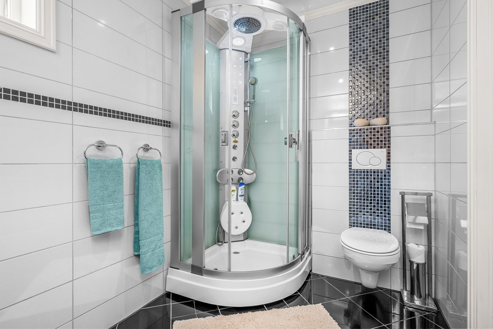 Badet er utstyrt med servantskap, dusjkabinett og veggmontert wc. Galleribilde