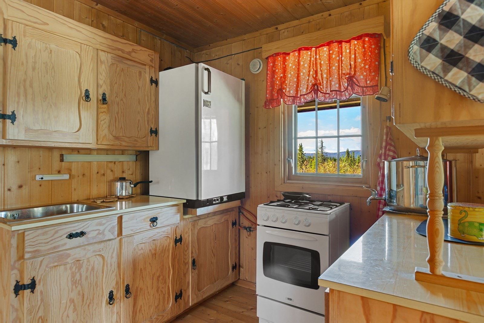 Her er plass til frittstående gasskomfyr og kjøleskap. Løsningen er både praktisk og koselig, med god arbeidsflate og nærhet til spiseplassen - perfekt for sosial matlaging. Galleribilde