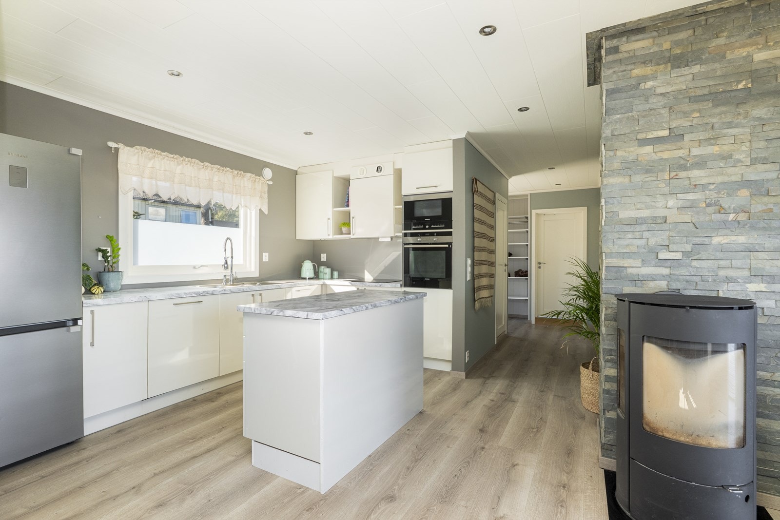 Vinduet over kjøkkenbenken tilfører godt med arbeidslys inn på kjøkkenet. Kjøkkenet har en hvit, tidløs innredning med innslag av åpne hyller, og det er gode arbeidsflater på laminerte benkeplater. Galleribilde