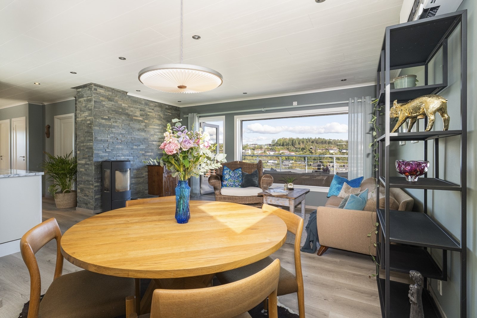 Ny vedovn fra 2022 med glassfelt på flere sider for lun varme på kjølige dager. Bak ovnen er det kledd med en flott skifer/steinpanel som gir et livfullt innslag i stua. Galleribilde