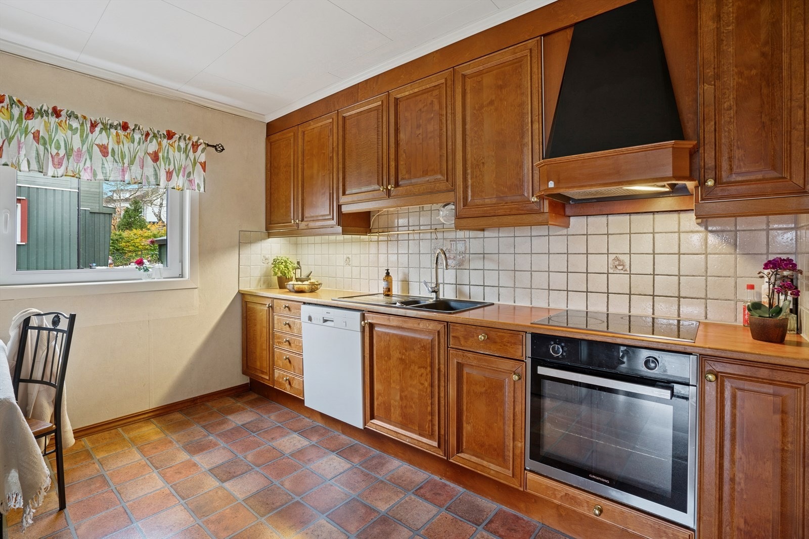 Det er fliser mellom benk og overskap, som beskytter veggen mot matsøl. Kjøkkenet er innredet med komfyr, platetopp, avtrekksvifte, oppvaskmaskin og plass til kjøleskap. Galleribilde