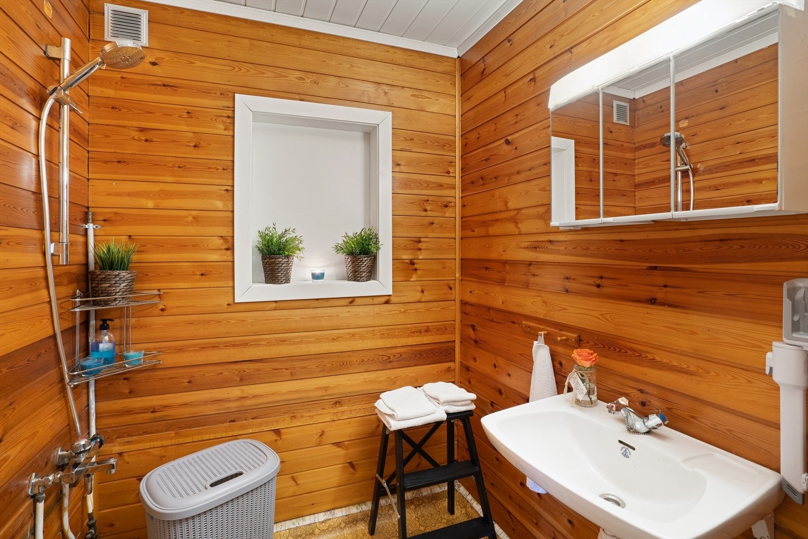 Baderommet i 1.etasje er fra 1987 ifølge eier. Det er innredet med WC på sokkel, dusjarmatur og servant, og har panel på tak og vegger, og belegg på gulvene. Galleribilde