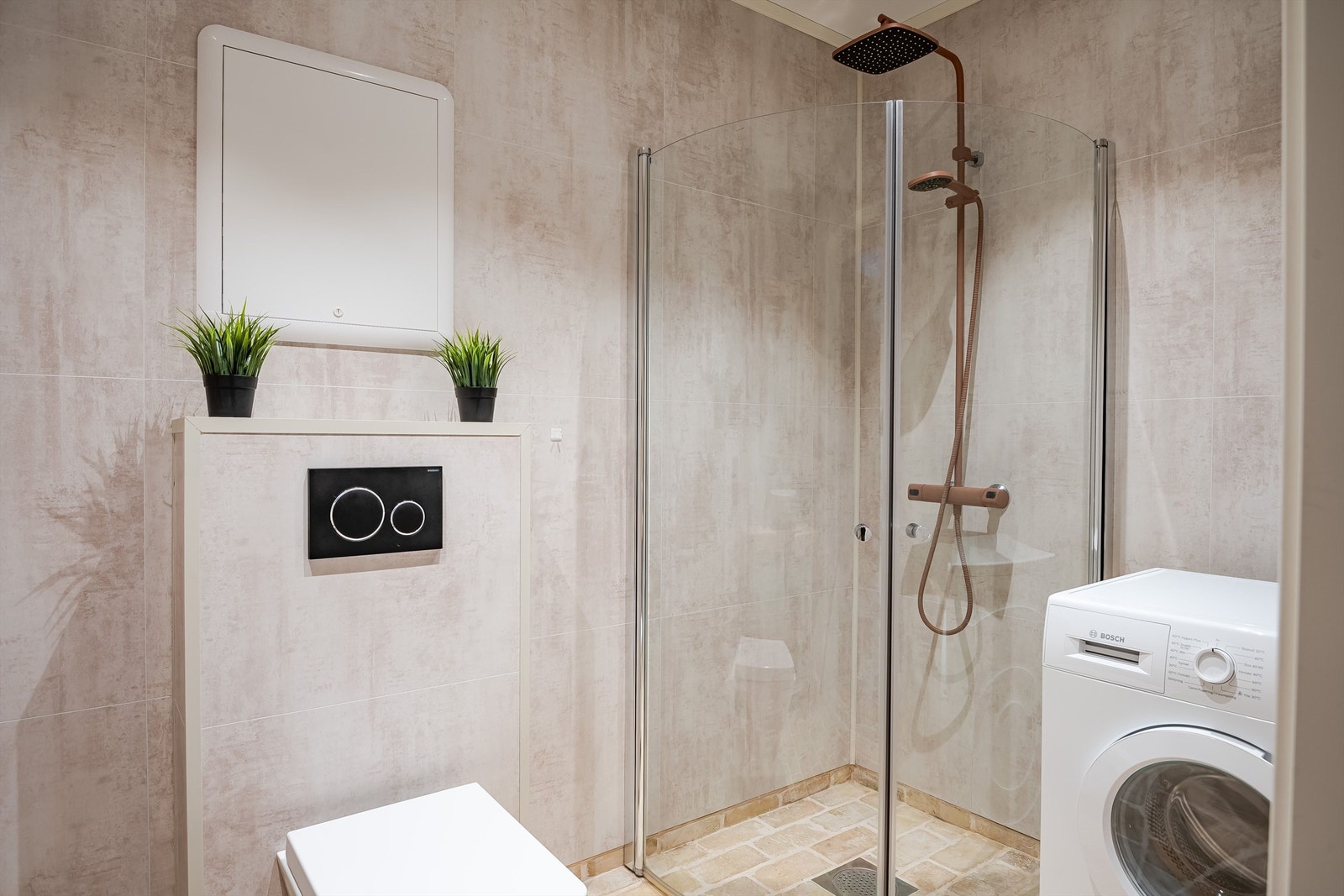 Tidsriktige våtromsplater på veggene, dusjhjørne med glassdører, vegghengt toalett og opplegg for vaskemaskin. Galleribilde